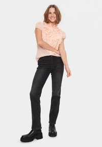 Blusa rosa chiaro con dettagli arricciati sul davanti, maniche a sbuffo corte, abbinata a jeans scuri e stivali neri chunky. Design semplice e pulito.