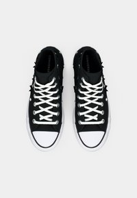 Μαύρα ψηλά αθλητικά παπούτσια με άσπρες κορδόνες και καουτσούκ σόλες, με υφή μαύρου υλικού και προεξέχουσες μαύρες ακίδες στο επάνω μέρος.