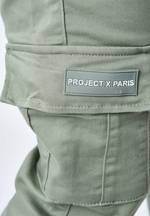 Pantaloni cargo verde oliva con una texture liscia, caratterizzati da un design a tasche sovrapposte e un patch in gomma etichettato "PROJECT X PARIS".