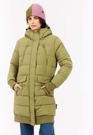 Vrouw in een groene gewatteerde jas met capuchon, met handen in de zakken, en een roze en olijfgroene brei-beret tegen een witte achtergrond.