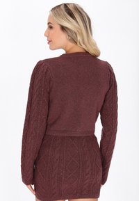 Bordo krótki sweter z teksturowanym wzorem w warkocze i długimi bufkami. Materiał delikatnie błyszczy. Posiada dopasowany krój w talii.