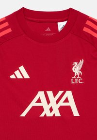 Punane lühikeste varrukatega spordisärk, millel on valge "L.F.C." vapp ja "AXA" logo. Õlgadel roosad Adidas'i kolmekordse triibuga disain. Sile tekstuur.