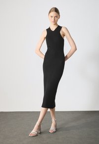 Musta ribbitty neulemekko, jossa on slim-fit -silhuetti, v-kaula-aukko ja puolipitkä pituus, yhdistettynä hopeisiin remmillisiin korkokenkiin.