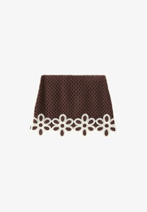Mini-jupe marron en crochet avec un bord en dentelle blanche en forme de fleur le long de l’ourlet, présentant un motif carré texturé sur toute la surface du tissu.