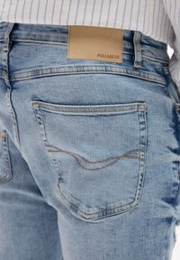 Svijetloplave traperice s kože etikete Pull&Bear. Karakteristike uključuju stražnje džepove i kontrastne detalje šavova.