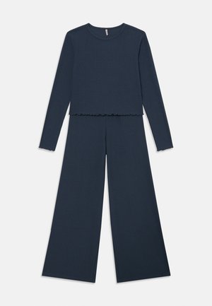 Námornícky modrý rebrovaný pletený top s dlhým rukávom a okrajom vo forme šalátu, skombinovaný s zodpovedajúcimi vysokými širokými nohavicami.