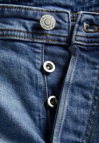 Close-up van blauwe spijkerbroek met metalen knoop en gedeeltelijk vastgemaakte gulp met knopen.