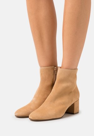 Beige semišové kotníkové boty se čtveratou špičkou, nízkým blokovým podpatkem a bočním zipem pro snadné obutí. Hladká textura a čistý design.