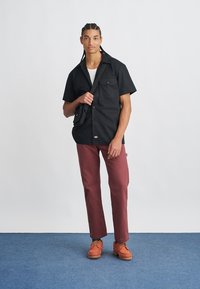 Mustade lühikeste varrukatega särk kahe rinnataskuga, burgundia värvi püksid ja oranžid batoonotsad tekstuursete tallaga. Üksikasjalik taust.