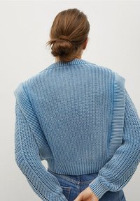 Pull bleu clair en tricot avec un dos texturé, des poignets côtelés et de larges accents aux épaules. Le design présente une coupe décontractée.