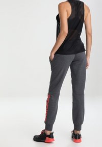 Zwarte mesh tanktop met een ontspannen pasvorm, gecombineerd met grijze joggers met rode "Adidas"-tekst en elastische boorden. Zwarte sportschoenen met rode accenten.