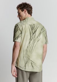 Korte mouwen shirt van zacht, lichtgroen stof met een gestructureerd uiterlijk, met een graspatroon en een knoopdetail op de rug.