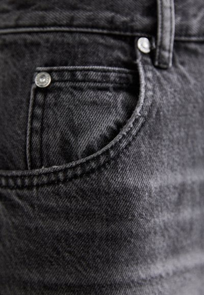 Črne jeans hlače iz denima imajo sprednji žep s srebrnim zakovicami, rahlo teksturo in kontrastno šivanje ob robovih.