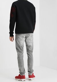 Svart tröja med röd blommig brodyr på ärmarna, grå tapered jeans och röda sneakers med vita sulor.