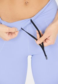 Ljuslila leggings med en slät textur, utrustade med ett svart snörningssystem i midjan för justerbar passform.