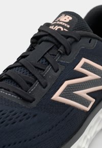 Black athletic shoe with a textured mesh upper, lace closure, and a contrasting rose gold logo. Features a cushioned white sole.