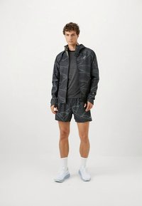Schwarze Sportjacke mit strukturiertem Muster, graues T-Shirt und passende Shorts mit Muster. Die Schuhe sind weiß mit hellblauen Akzenten.