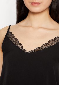 Camisole noire à encolure en V, ornée d'une bordure en dentelle délicate le long des bords et de fines bretelles réglables, fabriquée en tissu doux.