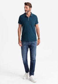 Tmavě modré polo tričko s bílými detaily, kombinované s modrými džíny a bílými teniskami. Polo má klasický límeček a přiléhavý střih.