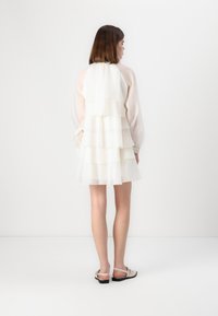 Rochie albă cu straturi și mâneci transparente, având trei volane orizontale. Material ușor, siluetă evazată, asortată cu sandale deschise.