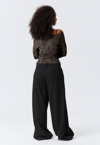 Long-sleeve, off-the-shoulder top in dark brown with a textured pattern, paired with loose-fitting black trousers featuring back pockets.