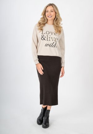 Beiger Pullover mit dem Aufdruck "Love & live wild" in Schwarz und Leopardenmuster. Dunkel gerippter Midirock und schwarze Knöchelstiefel.