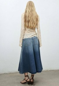 Denimrok met een uitlopende vorm en een licht-tot-donker verloop, gecombineerd met een textuur rijk, lichtgekleurde top en bruin sandaaltjes met hakken.