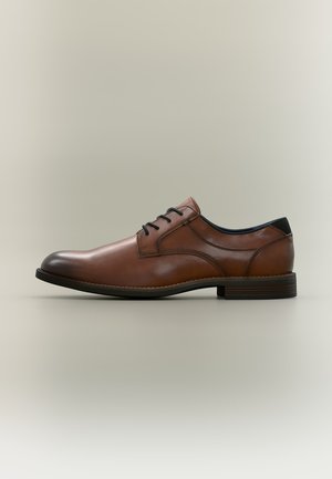 Chaussure de ville homme en cuir marron avec lacets noirs et petit talon, montrée de profil sur un fond neutre.
