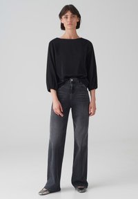 Schwarzes, locker sitzendes Langarm-Oberteil mit quadratischem Ausschnitt, kombiniert mit hochgeschnittenen, dunkelgrauen, weiten Jeans und silbernen Ballerinas.