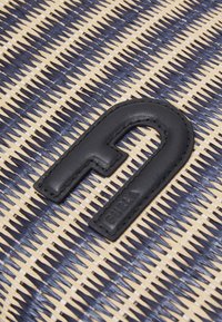 Woven fabric showing navy blue and cream patterns, with a black leather logo tag featuring a curved design and embossed text.