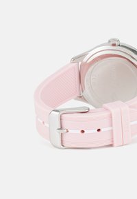 Bracelet de montre en silicone rose avec des rayures blanches, boucle en métal argenté et boîtier en acier inoxydable rond. Surface texturée et détails en relief.