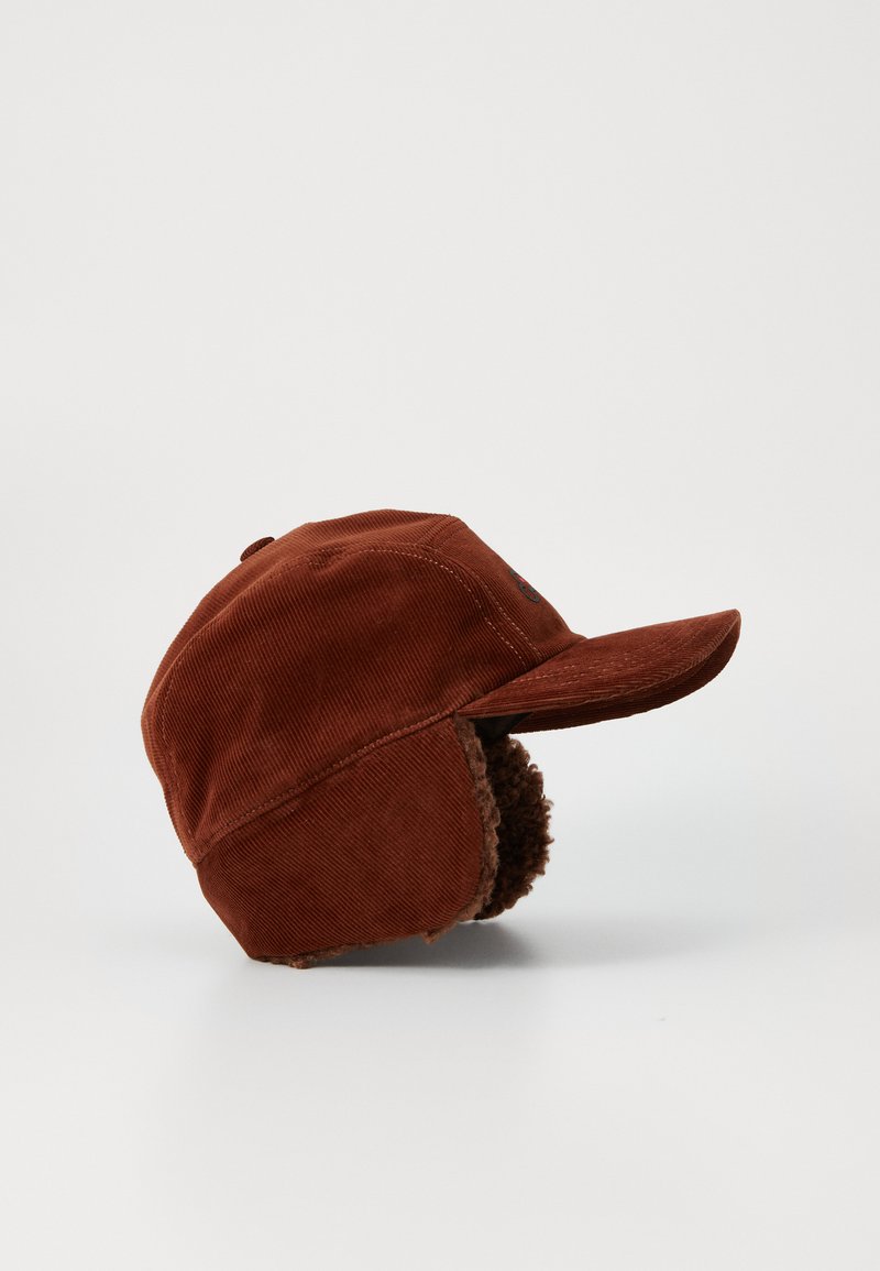 Brown corduroy cap with a curved visor and ear flaps lined with fluffy material. Features stitching on the crown and side logo detail.