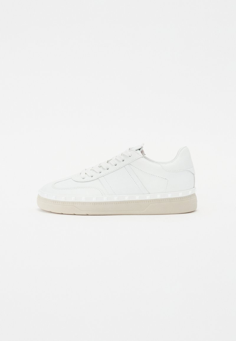 Baskets en cuir blanc avec une texture lisse, bout rond, design à lacets, semelle en caoutchouc de couleur claire et accents latéraux subtils pour le détail.