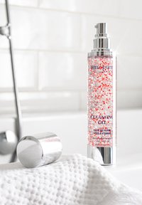 Rensende gel i en klar cylindrisk flaske med en sølv pumpe. Indeholder røde perler, mærket med produktinformation. Sølvhætte på et struktureret hvidt håndklæde.
