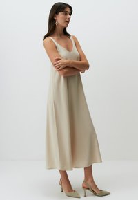 Abito maxi beige con scollatura a V e spalline sottili, realizzato in un tessuto liscio, caratterizzato da una vestibilità ampia e una silhouette fluida.