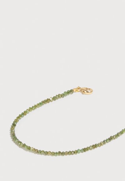 Λεπτό κολιέ με μικρές πράσινες πελεκητές χάντρες και χρυσό κούμπωμα σε λευκό φόντο.