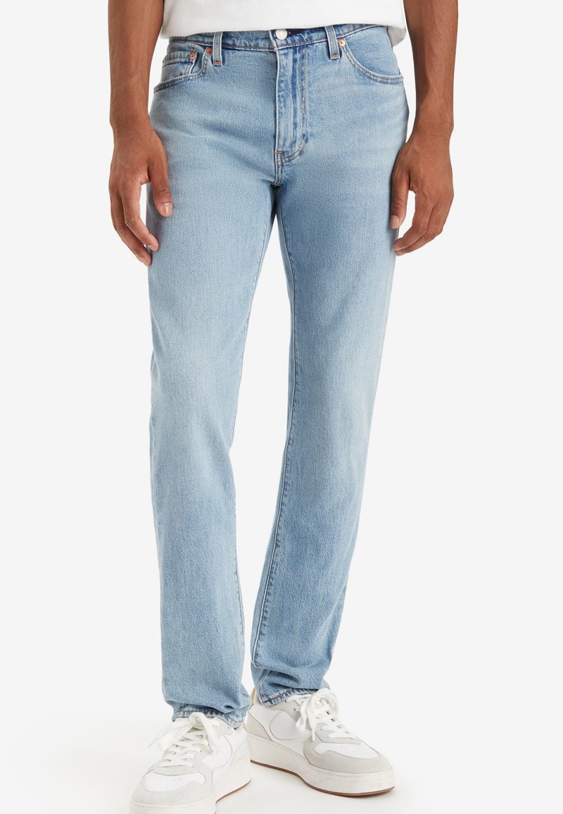 Lichtblauwe denim jeans met een recht model, gestikte details en een vijf-pocketontwerp, gecombineerd met witte sneakers. Glad textuur.