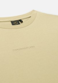 Lichtbeige katoenen T-shirt met een ronde hals, voorzien van een subtiel reliëflogo "TOMORROWLAND" op de voorkant. Glad textuur.