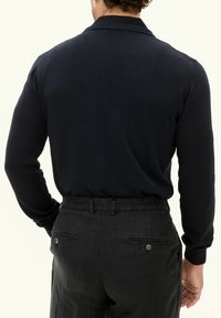 Navy gestrickter Pullover mit ribbeltem Kragen und Bündchen, kombiniert mit dunkelgrauen Hosen mit zwei Gesäßtaschen und Knopfdetails.