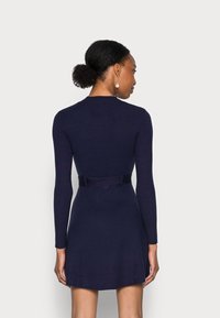 Marineblaues langärmliges Kleid mit einem figurbetonten Oberteil, schwingendem Rock und einem Stoffgürtel in der Taille. Glatte Textur und minimale Details.