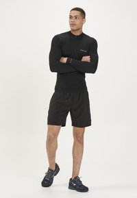 Långärmad svart träningsblus med dragkedja, kombinerad med svarta shorts och svarta löparskor med strukturerad ovandel och mesh-detaljer.