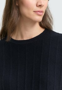 Marineblauer Strickpullover mit geripptem Muster, Rundhalsausschnitt und weichen Stoffdetails, die subtile Variationen in Schatten und Licht zeigen.