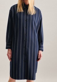 Mörkblå skjortklänning gjord av mjukt tyg, med vertikala vita ränder, krage och knappstängning framtill samt långa ärmar.