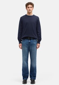 Granatowy sweter z długim rękawem i okrągłym dekoltem, zestawiony z jasnoniebieskimi jeansami o prostych nogawkach oraz czarnymi butami, noszony przez męskiego modela.