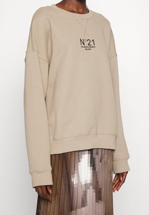 Beżowa, oversize bluza z napisem „N°21 VIA SANTO SPIRITO MILANO”, noszona z plisowaną spódnicą w pikselowy brązowo-biały wzór.