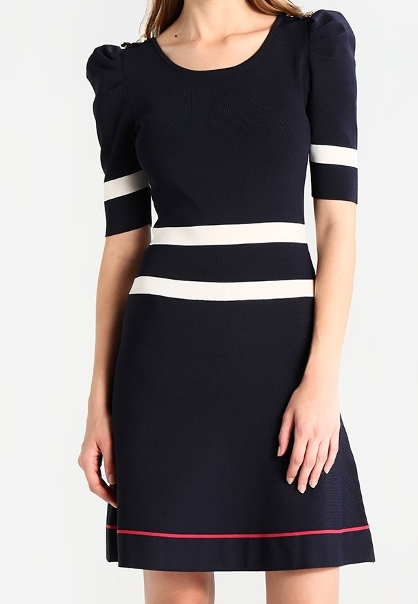 Femme portant une robe bleu marine avec des manches courtes bouffantes, des rayures horizontales blanches sur les manches et la taille, et une fine rayure rouge près de l'ourlet.