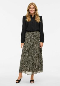 Chemise noire à manches longues avec des boutons à l'avant, associée à une jupe maxi fluide à imprimé léopard. Des talons ouverts noirs complètent la tenue.