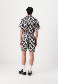 Korteærmet romper i creme med sort blomsterprint, elastisk talje og shorts. Har en foldet krave og bånd bagpå.