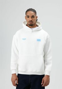 Witte hoodie van zachte stof met een kangoeroezak, geribbelde boorden en een capuchon met trekkoord. Voorzien van blauwe bedrukkingen.