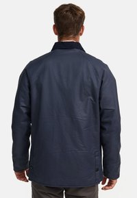 Veste bleu marine avec un col en velours côtelé, présentant une texture lisse, une coupe décontractée et des détails de boutons à l'ourlet et aux coutures latérales.